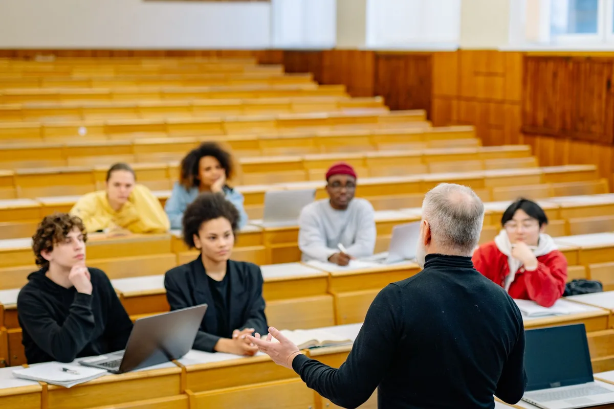 Profesor ense&ntilde;ando a estudiantes en un aula universitaria con diversidad de participantes.