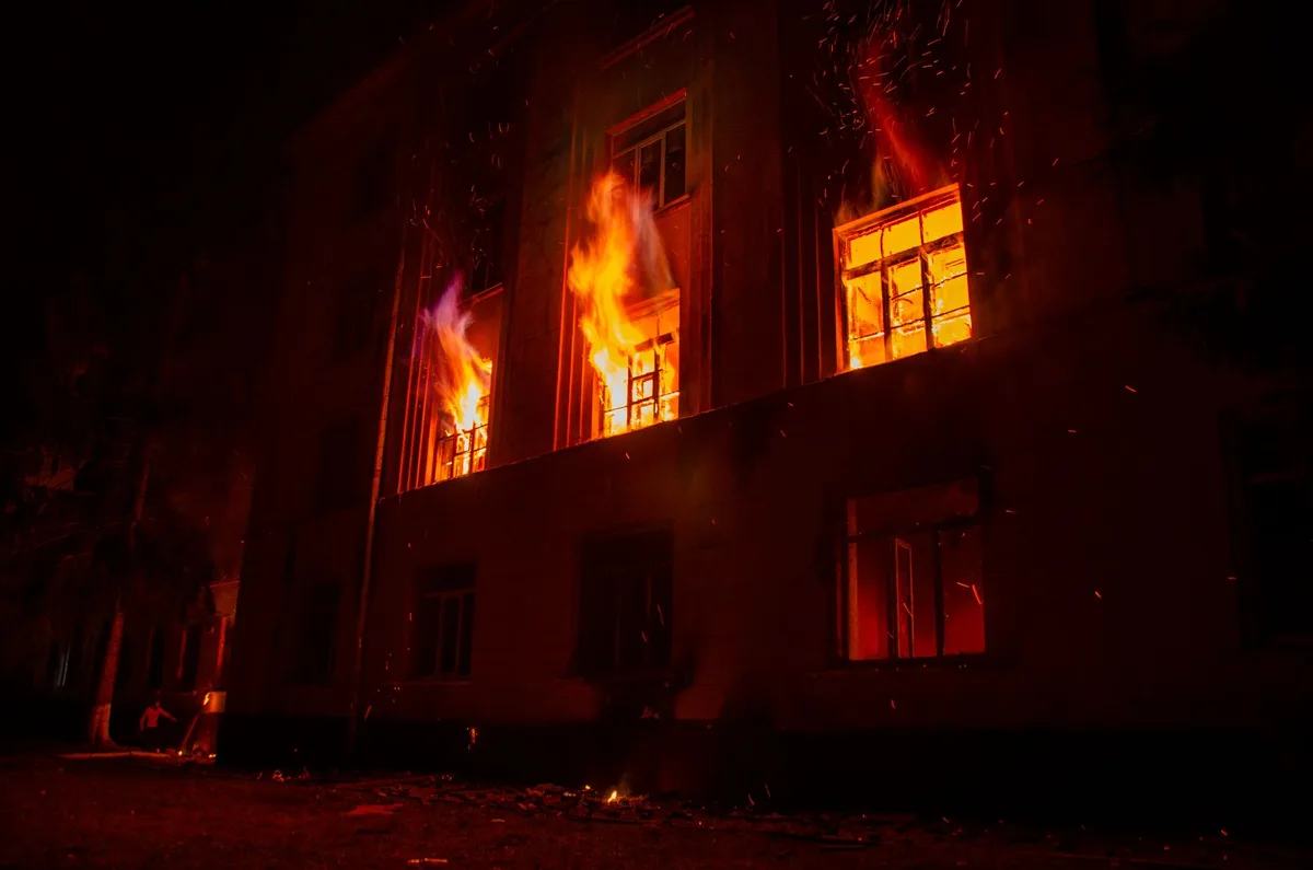 Firefighters in full gear responding to a residential house fire with emergency lights flashing in the background
