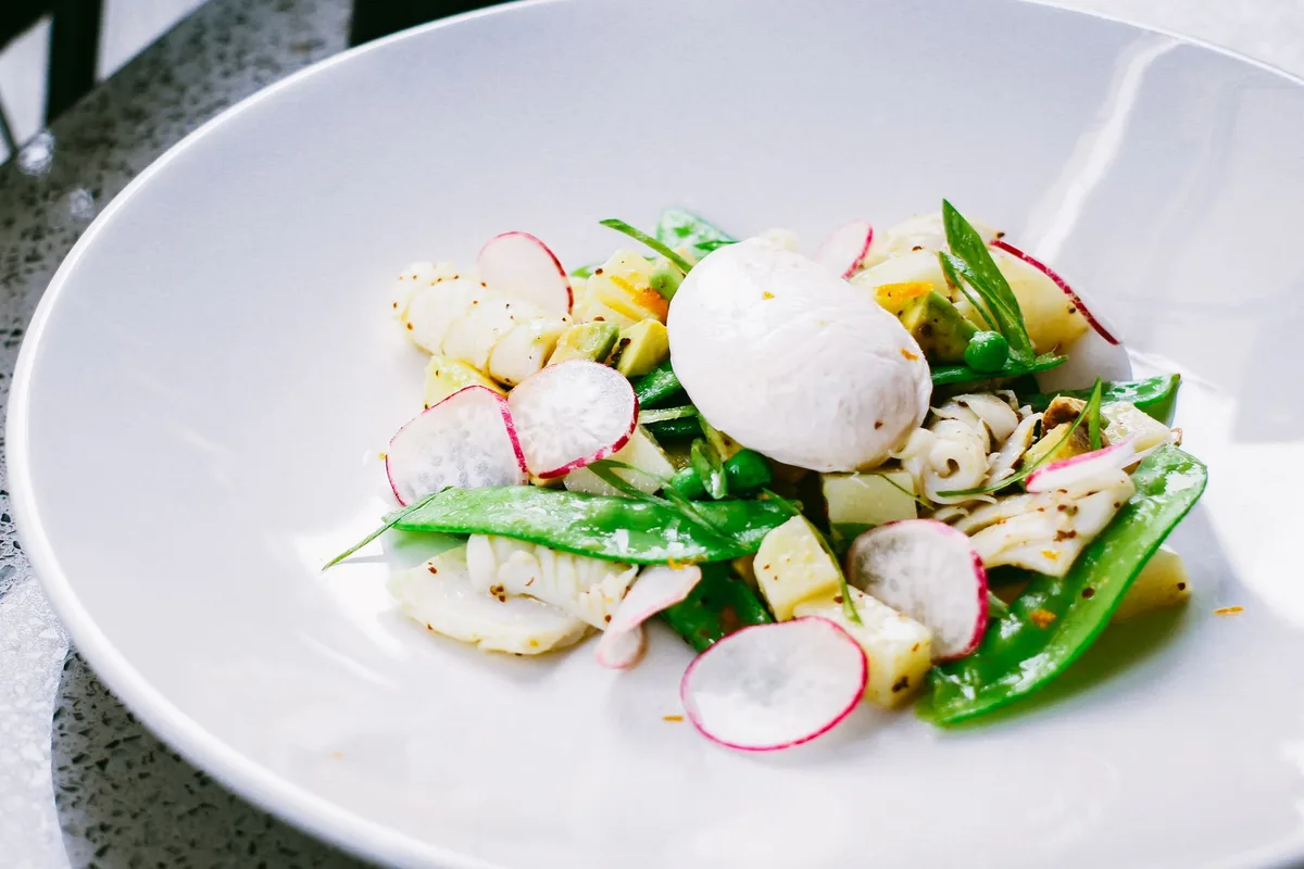 Spring salad bowl with fresh peas, young greens, and mint leaves on a white plate