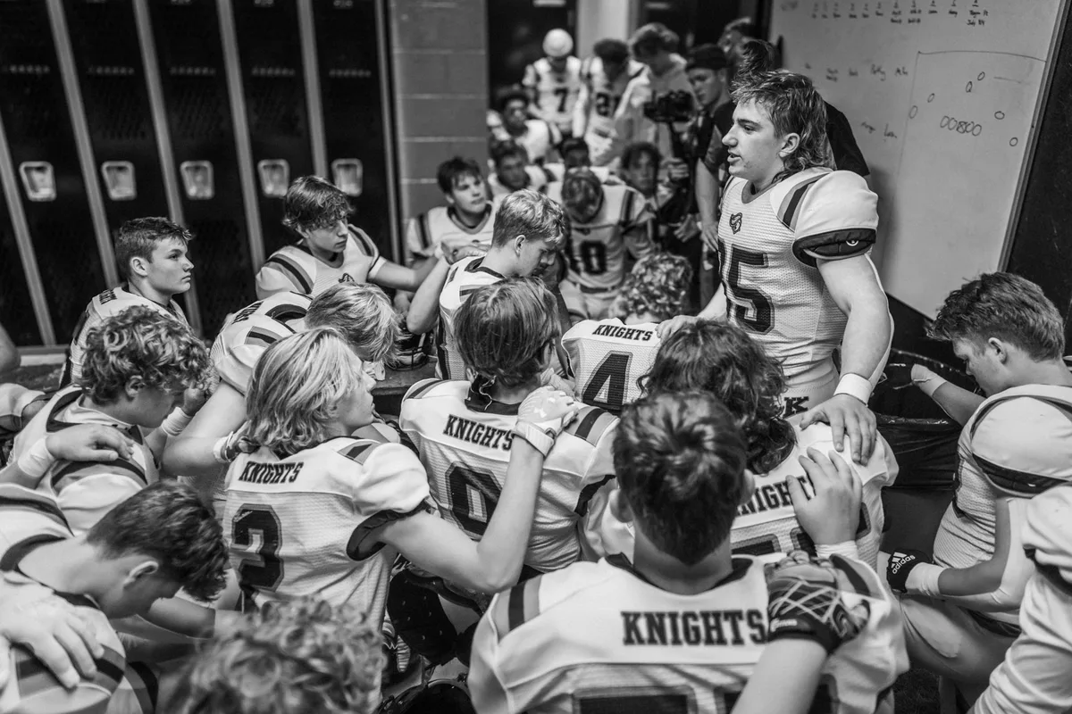 Coach and high school football players on sideline during opening game with stadium lights
