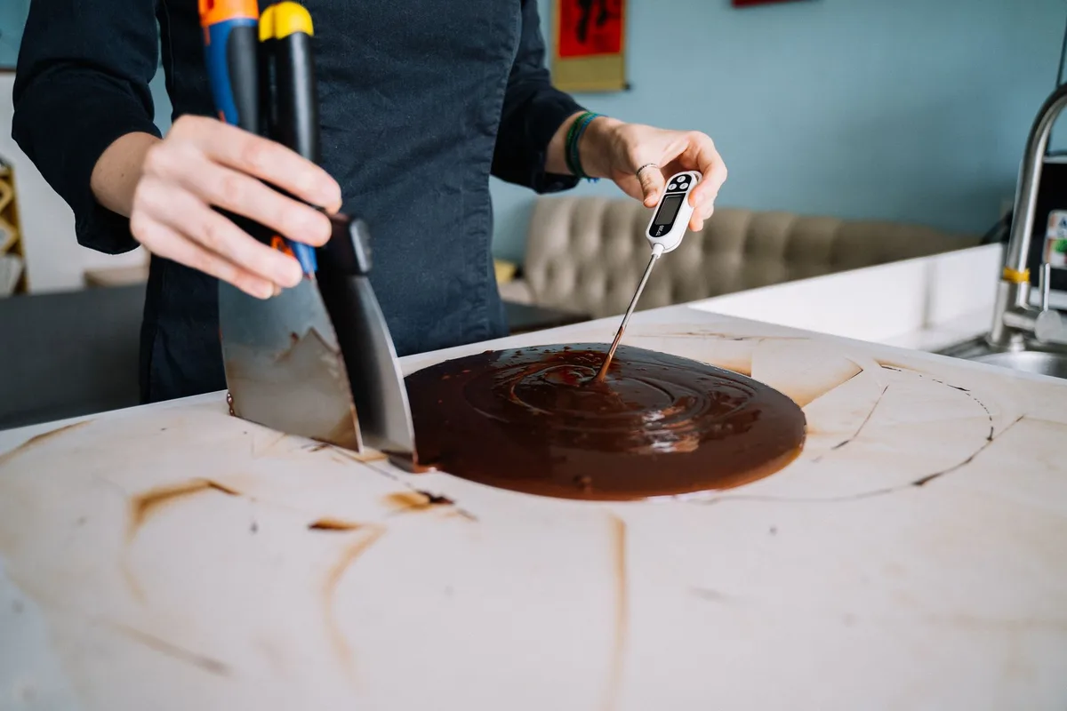 Candy thermometer clipped to a saucepan on a stovetop with sugar syrup heating