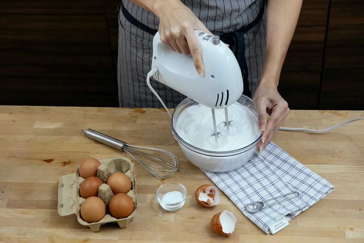 Electric mixer whipping egg whites to soft peaks in a metal bowl