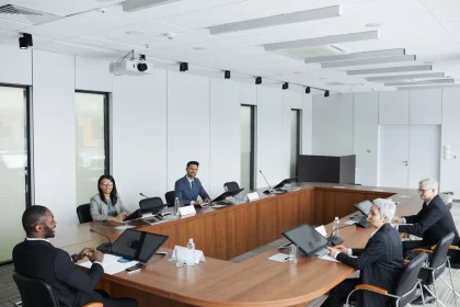 Business professionals and civic leaders in a collaborative meeting around a conference table with city skyline visible.