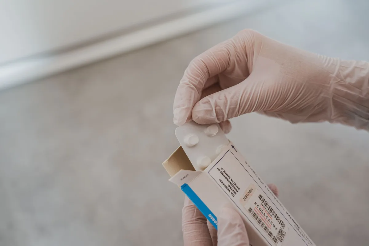 Hands holding a medication bottle at a mailbox, representing mail delivery of prescription drugs