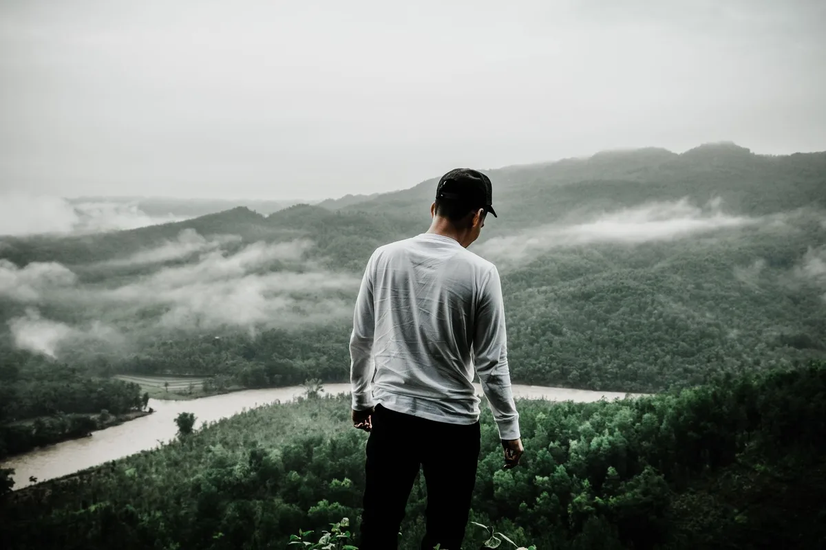 Person in protective long sleeves and pants hiking through brushy outdoor terrain.