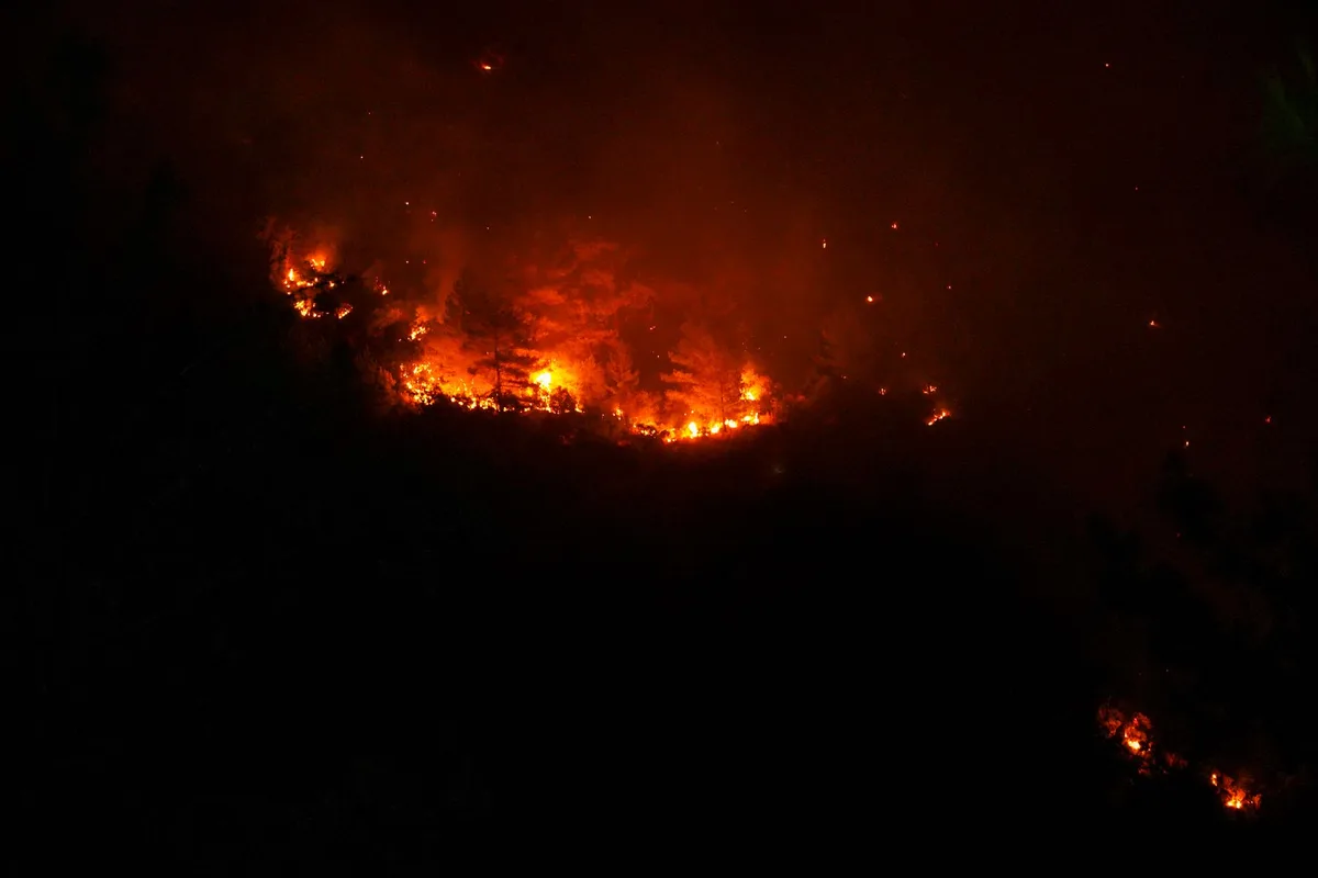 Firefighters battling a fast-moving wildfire threatening homes in dry grassland at evening