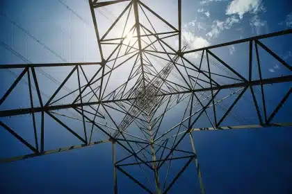 Gloved hands holding engineering plans with sunlit transmission towers visible through office windows