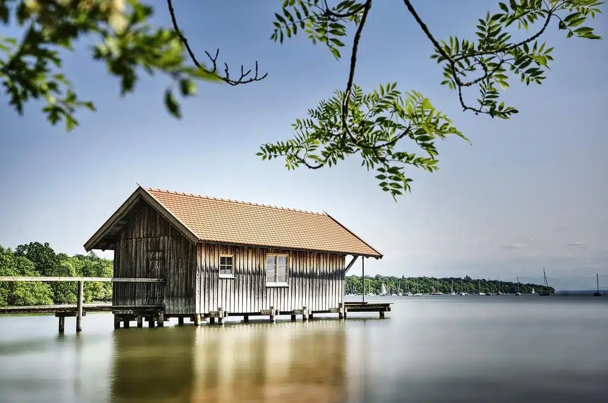 Boathouse and oars along a sunlit riverfront with people on the riverwalk