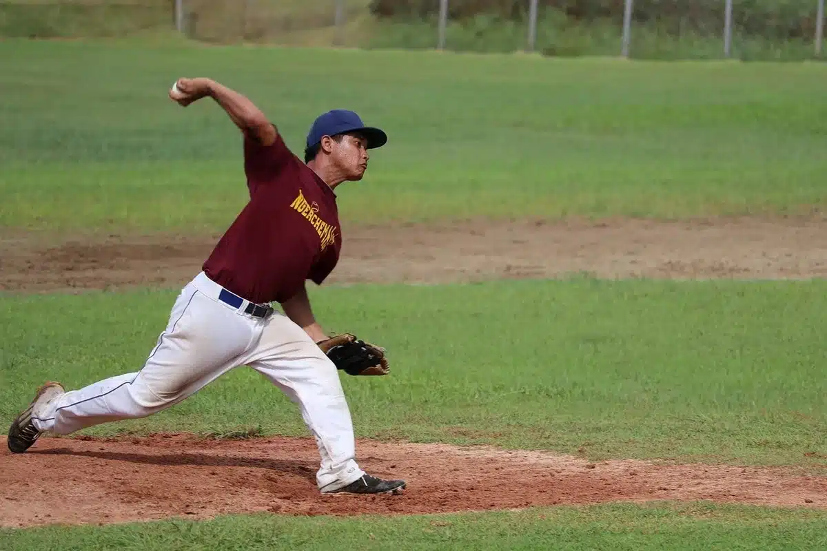High school two-way player swinging bat with pitcher warming in background