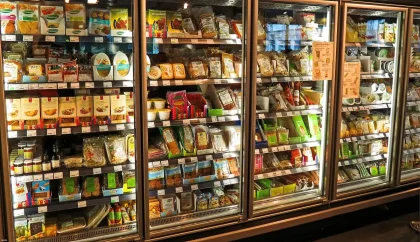 Shoppers reaching for frozen pizza boxes in a bright supermarket freezer aisle