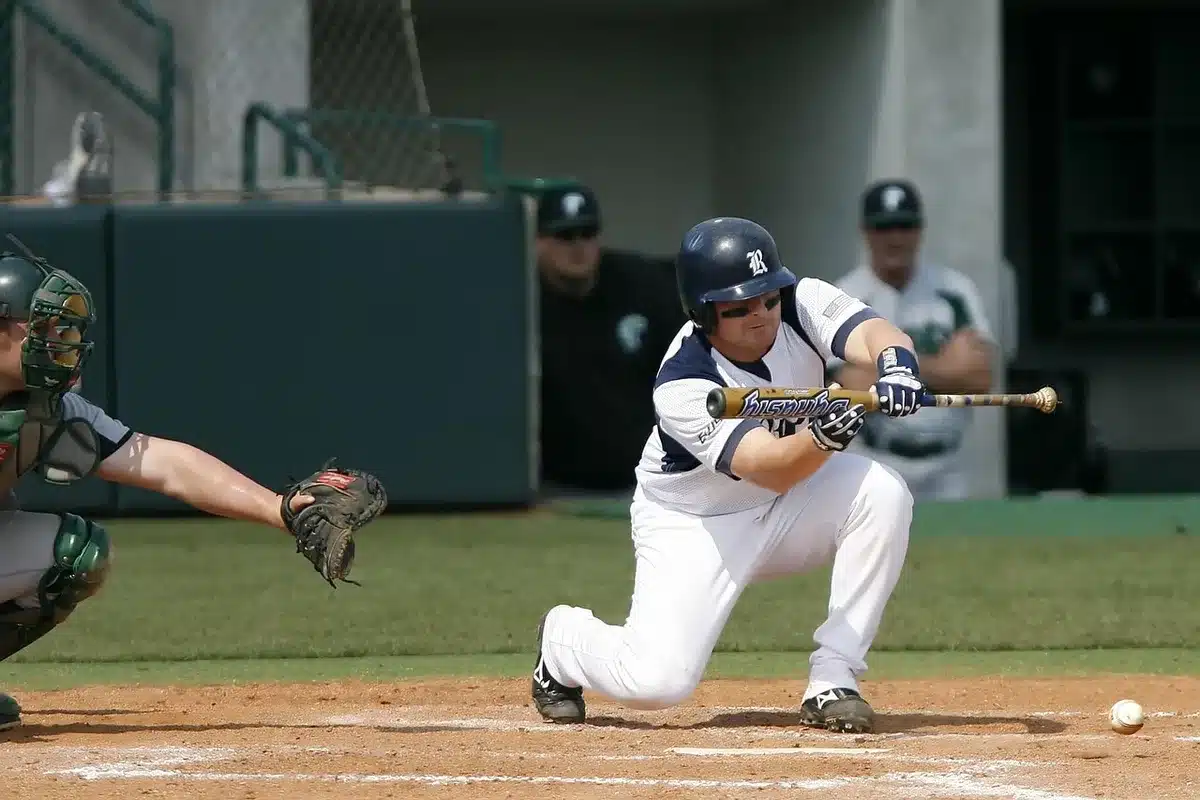 High-school batter stepping into the on-deck circle at a sunlit field