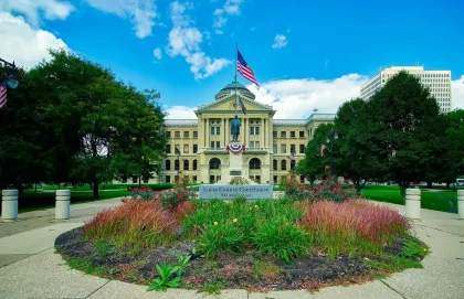 County courthouse lawn with investigators and an unmarked vehicle in daylight