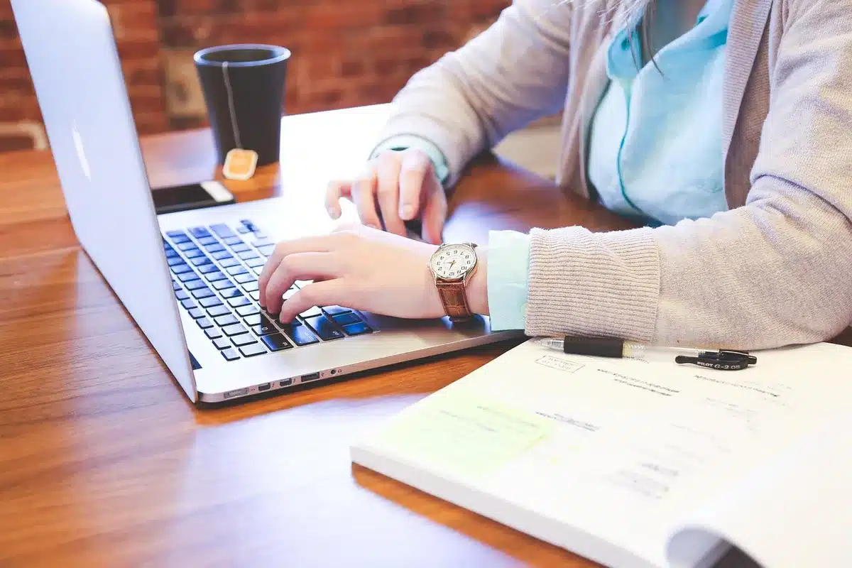 Sunlit office desk with laptop, notepad and hands poised to type